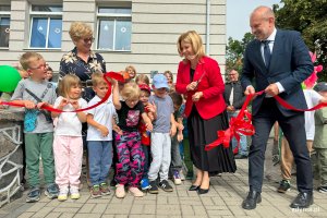 Trzy odsoby dorosłe w trakcie przecinana wstęgi z czerwona kokardą, wszędzie dookoła dzieci