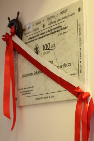 Przewiązana biało-czerwoną wstęgą biała tablica pamiątkowa z czarnymi literami przygotowana na stulecie Uniwersytetu Morskiego w kościele oo. Redemptorystów w Gdyni // fot. Martyna Kidoń-Olejarz