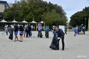 Po prawej: wiceprezydent Michał Guć zbiera odpady z gdyńskiej plaży w ramach akcji "Bałtycka Odyseja". W tle grupa wolontariuszy z workami i chwytakami w rękach // fot. Magdalena Czernek