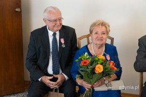 Mężczyzna w garniturze, kobieta w niebieskiej sukience z kwiatami w dłoni 