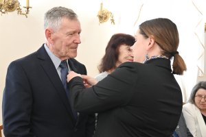 Kobieta w granatowej marynarce przypina medal starszemu mężczyźnie