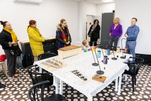 Przy stole z instrumentami muzycznymi siedzi dziecko, dookoła stoja kobiety.