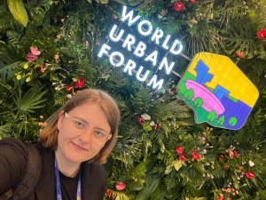 Joanna Kruczkowska z UrbanLab Gdynia na tle zieleni, powyżej świecący napis i grafika WUF