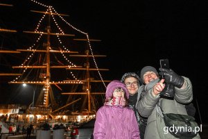 Mieszkańcy robiący sobie zdjęcie na tle świetlnej choinki na „Darze Młodzieży”