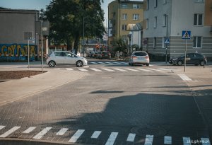 chodniki, wyniesione skrzyżowanie z kostki oraz przejścia dla pieszych po przebudowie. Widoczne oznakowanie, w tle budynki i tereny zielone