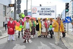 Uczestnicy przemarszu w ramach V Pomorskiego Dnia Seniora. W kolorowych strojach i z balonami w rękach. Dwie seniorki niosą transparent "Miejski Klub Seniora Witomino"