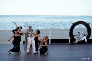 Grupa teatralna na scenie podczas przedstawienia, w tle morze i plaża