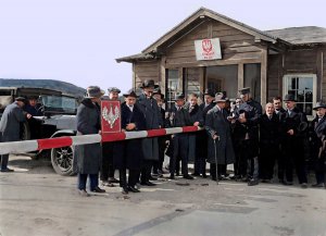 Grupa mężczyzn przy szlabanie i budynku strażnicy.