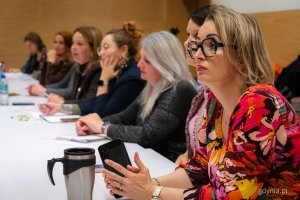 Kobiety przy stole, na pierwszym planie kobieta w kolorowej sukience.