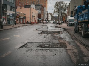 trwające naprawy nawierzchni, widoczne łatanie ubytków, w tle pojazdy