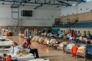 Dzieci na sali gimnastycznej z łóżkami przygotowanymi dla uchodźców