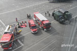 Strażacy i żołnierze stojący przy strażackich i wojskowych samochodach i ciężarówkach