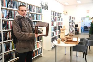 Młody mężczyzna z karmnikiem w ręce na tle książek