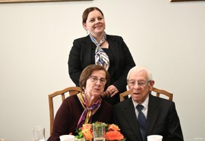 Para senior&oacute;w na krzesłach za nimi stoi kobieta w ciemnej marynarce