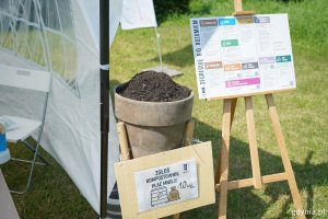 Donica z ziemią i tabliczka z napisem: zgłoś kompostownik, płać mnie
