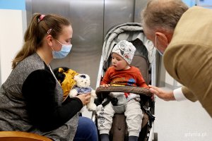 Prezydent Gdyni rozmawia na korytarzu szpitalnym z mamą małego dziecka, które siedzi w wózku.