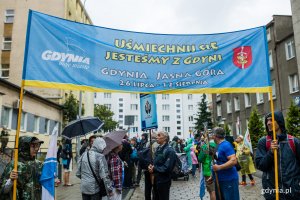 Uczestnicy 37. Gdyńskiej Pieszej Pielgrzymki na Jasną Górę przed kościołem Najświętszego Serca Pana Jezusa. Dwoje z nich (na pierwszym planie) trzyma baner z napisem "Uśmiechnij się, jesteśmy z Gdyni" // fot. Karol Stańczak