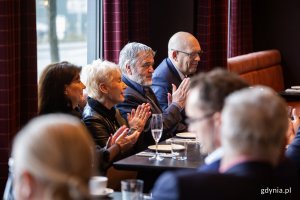 Ludzie przy stołach w restauracji biją brawo.