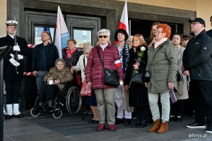 Uczestnicy obchod&oacute;w w okolicy tablicy pamiątkowej, kt&oacute;ra znajduje się na fasadzie Dworca PKP Gdynia Gł&oacute;wna, podczas uroczystości z okazji 87. rocznicy pierwszych wysiedleń Gdynian 