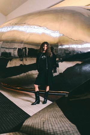 W kolekcji marki Diverse znalazły się między innymi T-shirty. Modelka w kręconych włosach pozuje w koszulce na tle sfery w Muzeum Emigracji w Gdyni