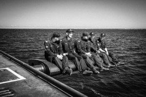 Czarno-białe zdjęcie przedstawiające marynarzy siedzących na sterze głębokości okrętu podwodnego