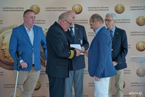 kpt. ż. w. Mariusz Wiktorowicz wręcza Nagrodę im. Kapitana Leszka Wiktorowicza kpt. Michałowi Bielskiemu. Za nimi (od lewej): radny Gdyni i członek kapituły Arkadiusz Dzierżyński, kpt. Marek Padjas z Bractwa Kaphornowc&oacute;w i Waldemar Heflich z Press Clubu Polska