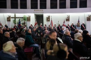 Ludzie siedzący w kościelnych ławach i stojący pomiędzy nimi