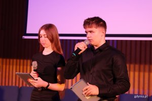 Para młodych ludzi  przemawiajacych przed widownią z mikrofonem w ręku