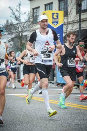 Mężczyzna w czarno-białym stroju sportowym biegnący po ulicach miasta w otoczeniu innych biegaczy