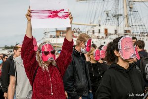 Uczestnicy akcji "Stop przemocy wobec narodu Białorusi" w maskach z podobizną aleksandra Łukaszenki. Po lewej stoi dziewczyna w czerwonej bluzce i okularach, trzyma w ręku kartkę w barwach naradowych Białorusi. Kreska koloru czerwonego wymalowana jest sztuczną krwią // fot. Karol Stańczak