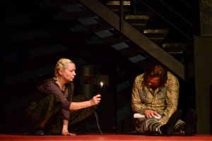 Zdjęcie z próby spektaklu „Misery” na podstawie powieści Stephena Kinga w reżyserii Krzysztofa Babickiego. Na fotografii: Dorota Lulka jako Annie Wilkes i Szymon Sędrowski jako Paul Sheldon. Annie trzyma w ręku zapaloną zapalniczkę. Paul siedzi skulony pod schodami // fot. Roman Jocher