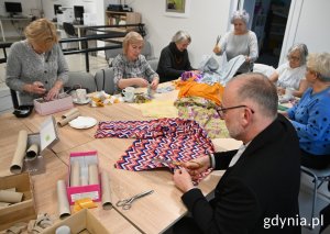 Seniorki i wiceprezydent Michał Guć przy stole przygotowują z materiałów i papierowych tutek zabawki dla kotów