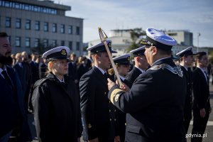 Rektor uczelni stoi z buławą przed studentami.