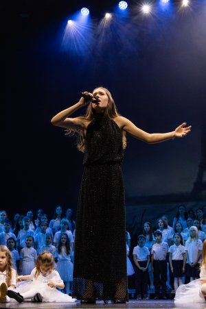 Młoda dziewczyna z mikrofonem w czarnej sukience na scenie