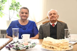 Starsza pani w niebieskiej bluzce i mężczyzna w garniturze przy stole 