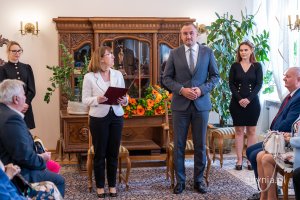 Kobieta w białej marynarce i mężczyzna w garniturze na tle kwiatów