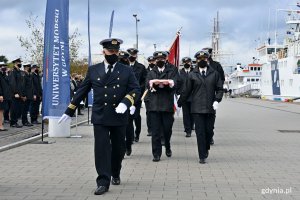 Poczet sztandarowy maszeruje wzdłuż nabrzeża. Pierwsza para niesie złożoną biało-czerwoną flagę // fot. Magdalena Czernek