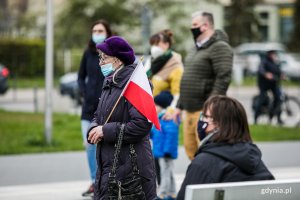 Gdynianka z biało-czerwoną flagą w ręce podczas uroczystości Dnia Flagi RP. W tle inni uczestnicy obchodów // fot. Karol Stańczak