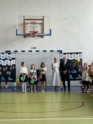 Uroczystość w hali sportowej na tle bramki dyrekcja placówki i dzieci podczas wystąpienia