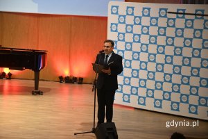 Mężczyzna elegancko ubrany stoi na scenie przed mikrofonem