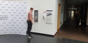 Mężczyzna w różowym T-shircie i czarnych spodniach korzysta z energooszczędnej tablicy z e-papieru zainstalowanej w PPNT Gdynia