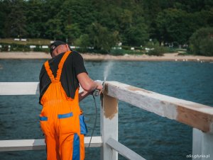 malowanie i szlifowanie drewnianych elementów mola, widoczni pracownicy wykonujący prace w odzieży ochronnej