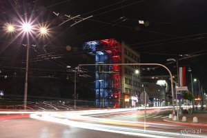 Budynek InfoBoksu oświetlony na biało-czerwono. Na pierwszym planie ruch uliczny i świecące latarnie // fot. Michał Puszczewicz