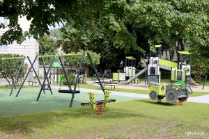 plac zabaw dla dzieci, na pierwszym tle huśtawki, po prawej traktor, w głębi bocianie gniazdo