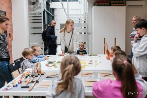 Kasia z projektu "Sianko" (blondynka stojąca przy stole, na środku) prowadząca warsztaty plastyczne dla dzieci. Przy stole siedzą mali uczestnicy zajęć // fot. Karol Stańczak