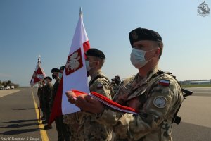 Żołnierze Polskiego Kontyngentu Wojskowego ustawieni w rzędzie. W rękach trzymają biało-czerwone flagi i sztandar // fot. K. Kamińska, S. Smuga/ BLMW