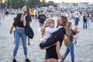 Kobieta tańczy na plaży z dzieckiem na rękach.