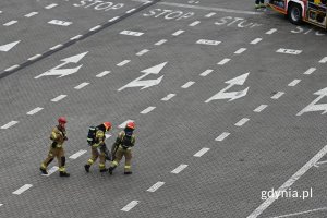 Strażacy niosący przez pusty parking poszkodowanego kierowcę samochodu osobowego