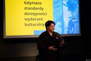 Anna Dobkowska z Wydziału Dostępności Urzędu Miasta Gdyni na tle prezentacji standard&oacute;w dostępności