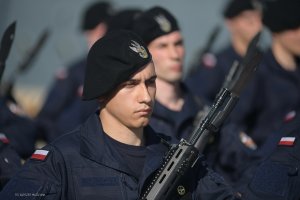 Szereg żołnierzy, na pierwszym planie młody marynarz z karabinem